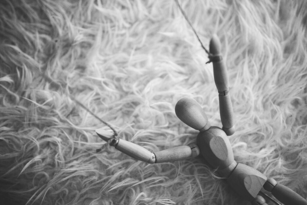 Black and white image of a wooden puppet laying on a furry surface, evoking a dramatic and artistic mood.