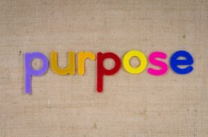 Colorful felt letters spelling 'purpose' on a textured fabric background with ample copyspace.